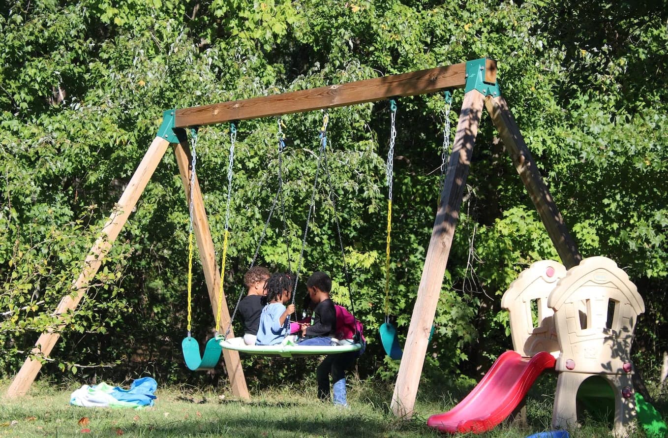 Kids sitting together on a round swing in the backyard, with a little slide beside it