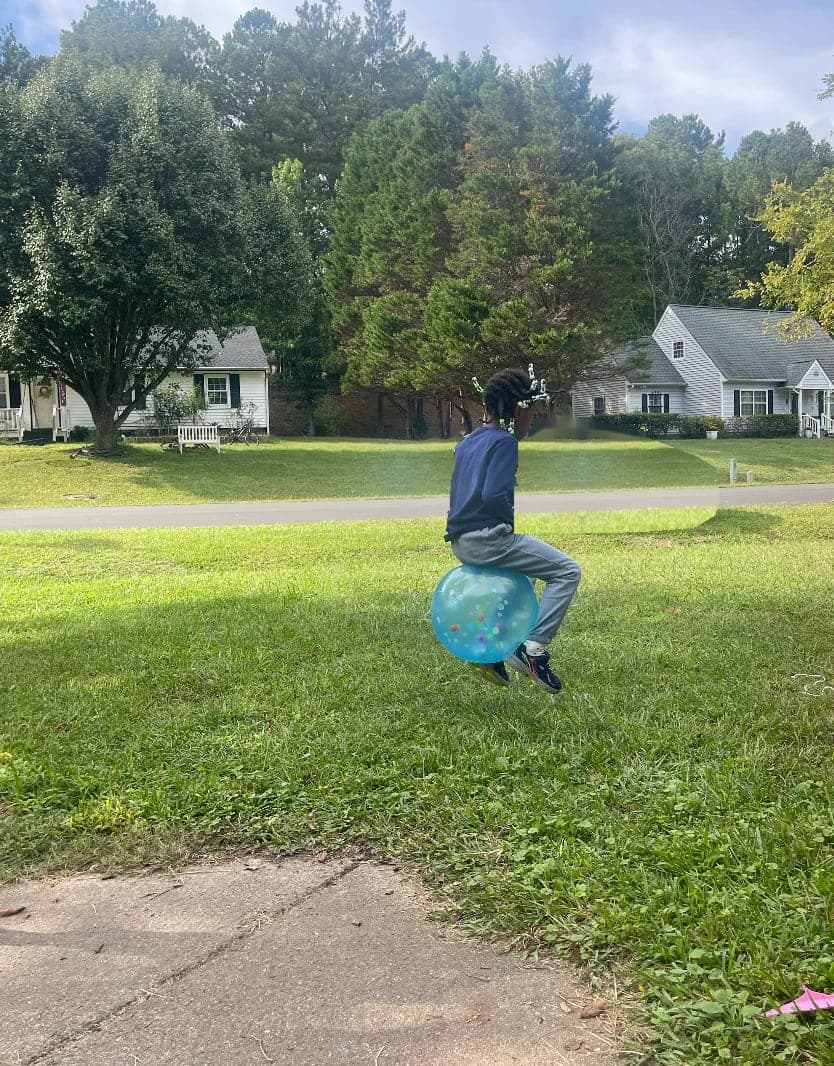 A child bouncing on a hopper ball on the lawn