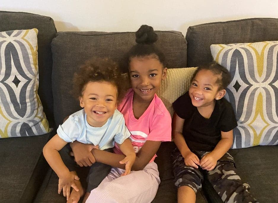 Three smiling kids snuggled together on the couch